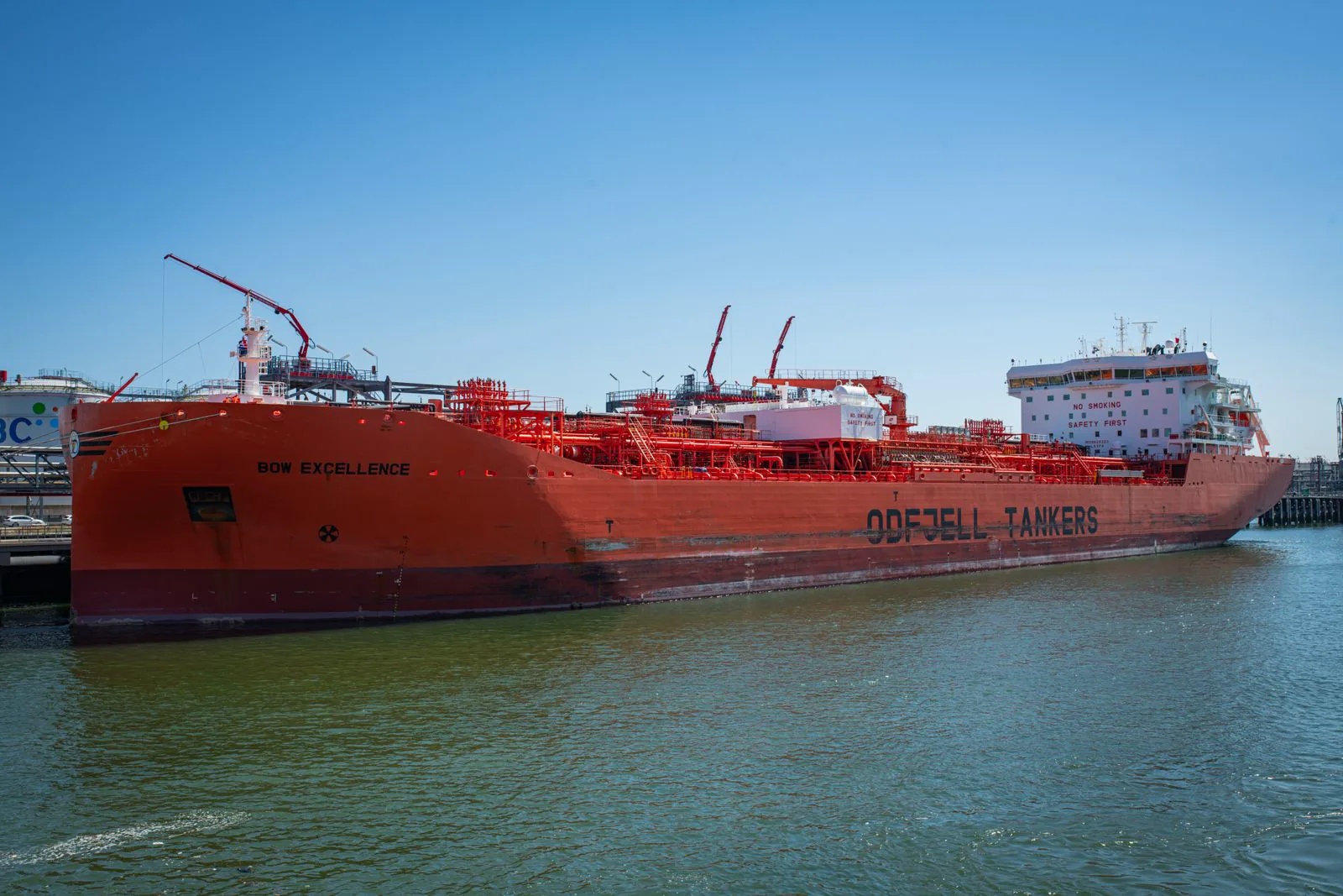 A large red oil tanker docked at an industrial harbor.